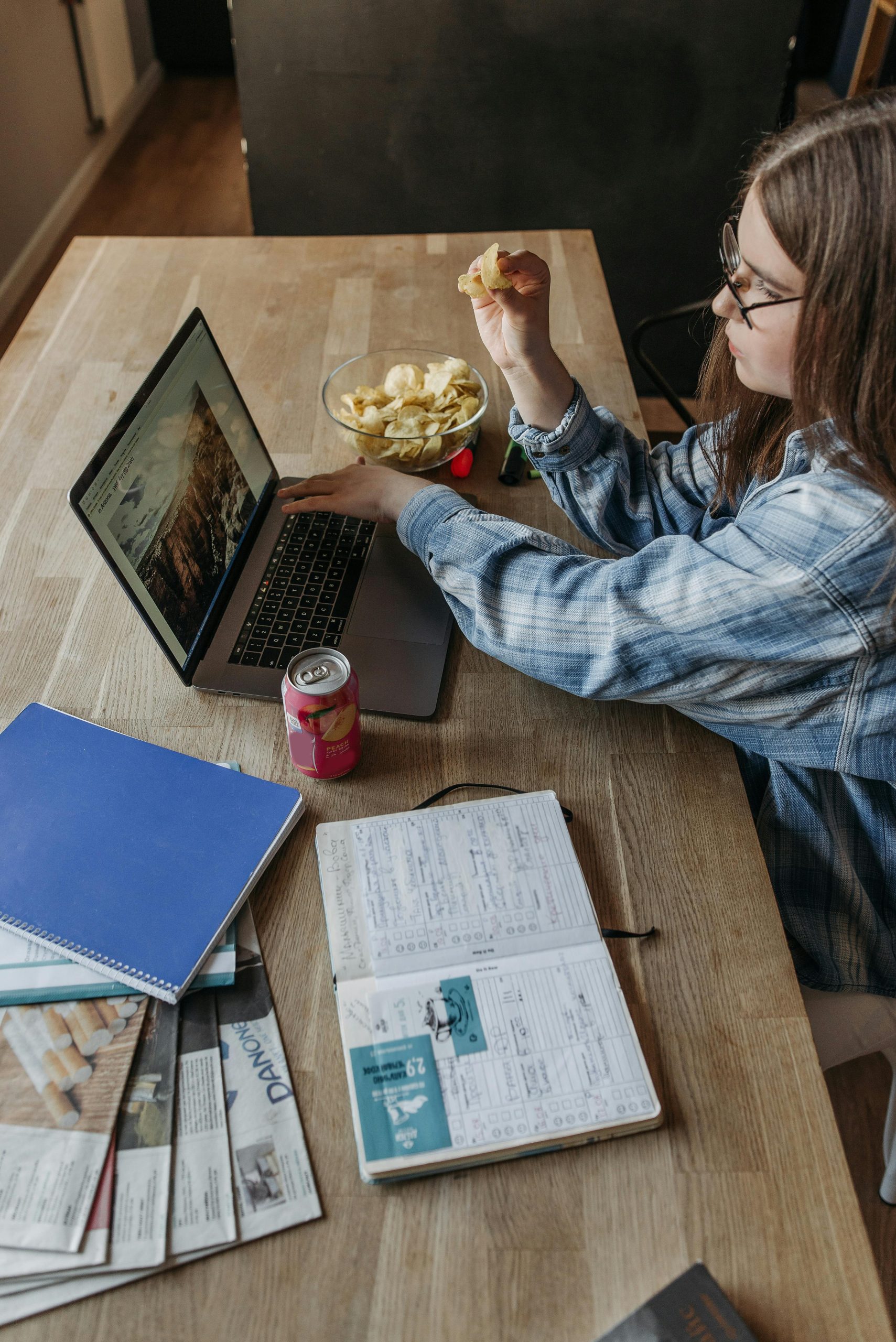 Woman working from home with a laptop, notebooks, and snacks on a table.