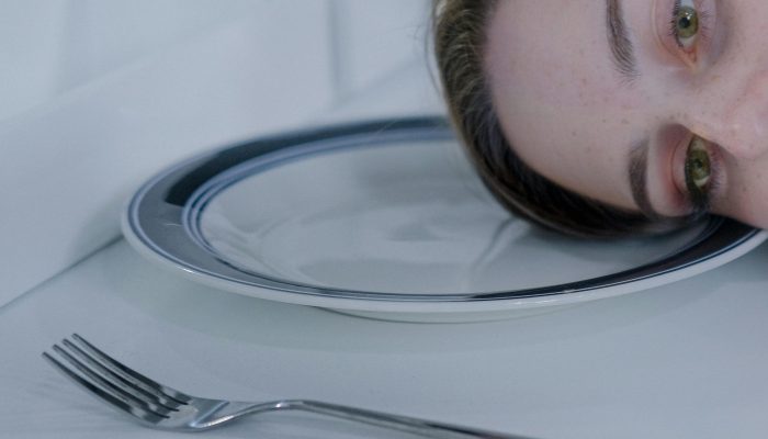 pexels photo 18371583 18371583 A woman rests her head on a plate next to a fork, exuding a contemplative mood.